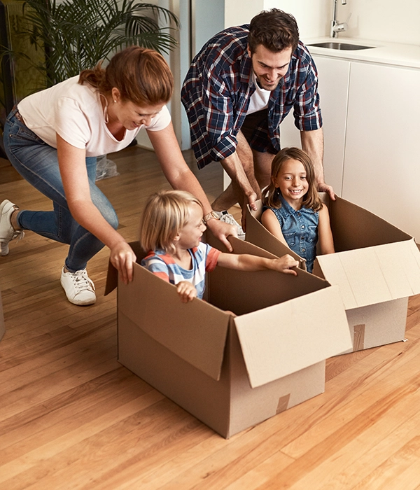 Unos padres jugando con sus hijos que están metidos en las cajas de mudanza.
