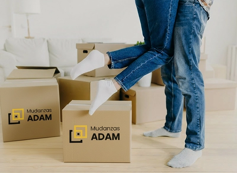 Imagen recortada donde se ven las piernas de una pareja y cajas serigrafiadas con el logo de Mudanzas Adam.