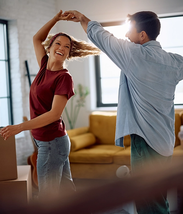Una pareja bailando en el salón de casa donde está con las cajas de mudanza.